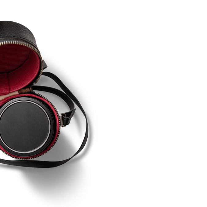 A round black leather case with a red interior lining, partially unzipped, showing a circular black object inside—perfect for storing small Mental Health Resources—set against a black background.